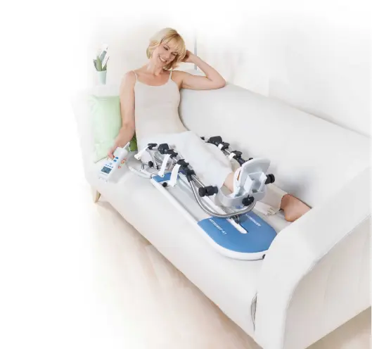 Une patiente utilise un arthromoteur de rééducation Kinetec en location, démontrant le confort d'utilisation à domicile sur un canapé blanc. L'image illustre la facilité d'accès aux équipements médicaux professionnels proposés par Medirent pour la rééducation à domicile.